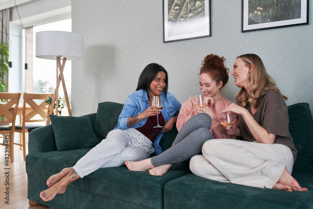 Three  female caucasian friends chatting and drinking wine at home