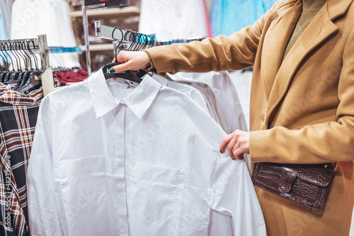 Female customer chooses clothes in a store, a blonde looks at a T-shirt in a boutique on a hanger, a woman buys on sale. The concept of shopping