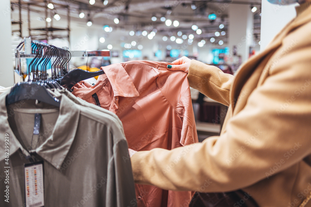 Female customer chooses clothes in a store, a blonde looks at a T-shirt in a boutique on a hanger, a woman buys on sale. The concept of shopping Female customer chooses clothes in a store, a blonde looks at a T-shirt in a boutique on a hanger, a woman buys on sale. The concept of shopping