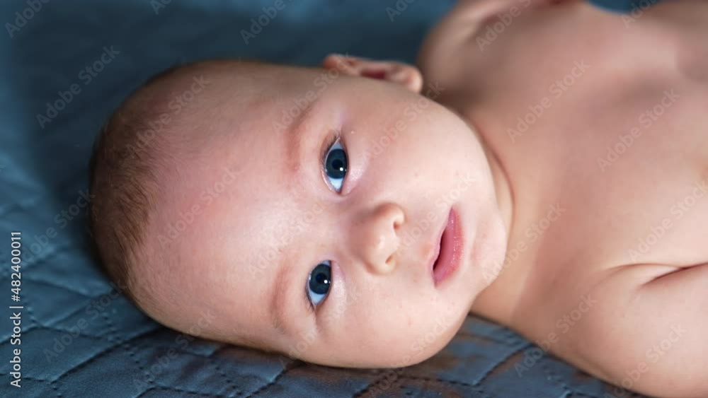Beautiful baby face staring in camera. Small kid trying to pronounce different sounds. Close up. Grey blanket backdrop. Beautiful baby face staring in camera. Small kid trying to pronounce different sounds. Close up. Grey blanket backdrop.