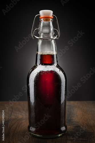 Flip top glass bottle puring fizzing bubbling dark soda over ice on a dark wood table top with dark background.