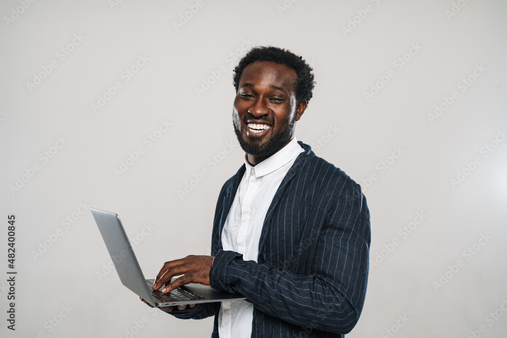 Young black man wearing jacket smiling while typing on laptop Young black man wearing jacket smiling while typing on laptop