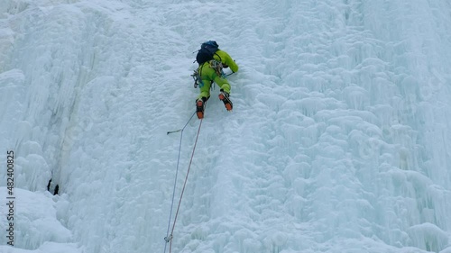 Alpinist man with ice tools axe climbing a frozen waterfall, a large wall of ice