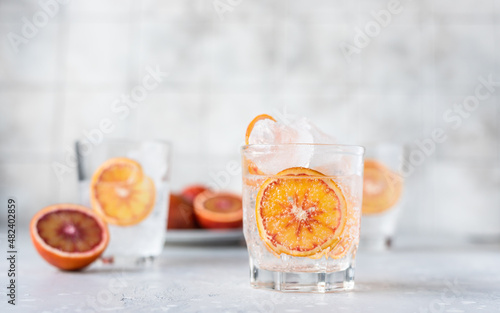 Tonic nonalcoholic mocktail with red Sicilian oranges and ice, grey background. Cold refreshing summer mojito lemonade.