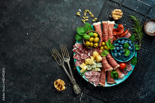 Italian snacks. Plate with cheese and ham, prosciutto, jamon salami, and snacks. On a black stone background.