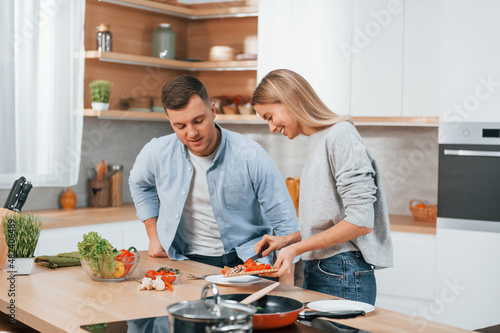 Using vegetables. Couple preparing food at home on the modern kitchen