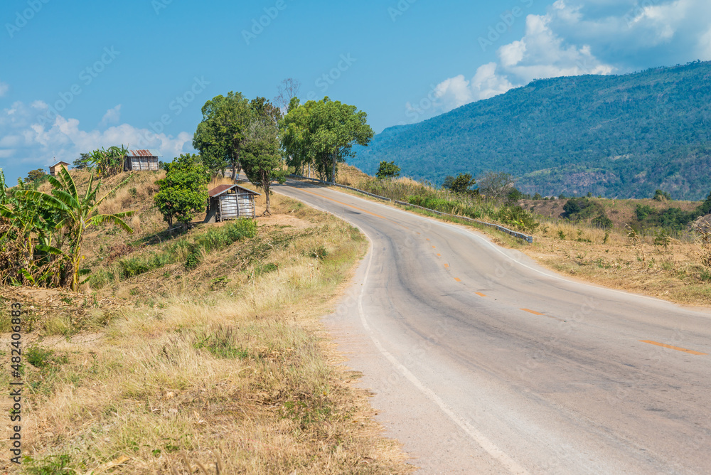 Beautiful asphalt country road side on the green mountain with blue sky background in sunny day, Phetchabun Thailand. Road trip, travel holiday or transportation concept.
