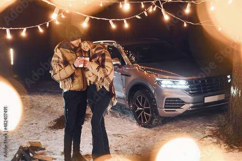 With warm drinks. Couple standing in the forest and celebrating New year