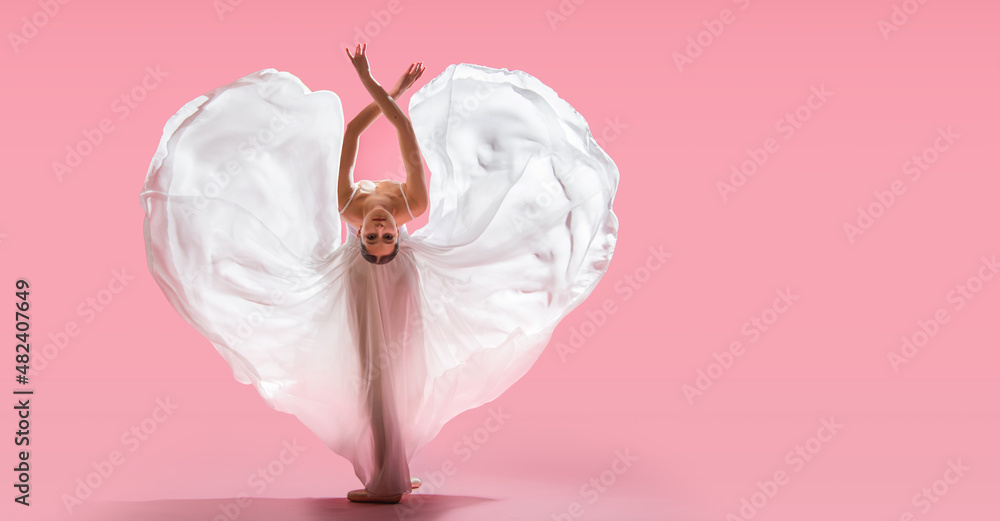 elegant ballerina in pointe shoes dancing in a long white skirt developing in the shape of a heart on a pink background - obrazy, fototapety, plakaty 