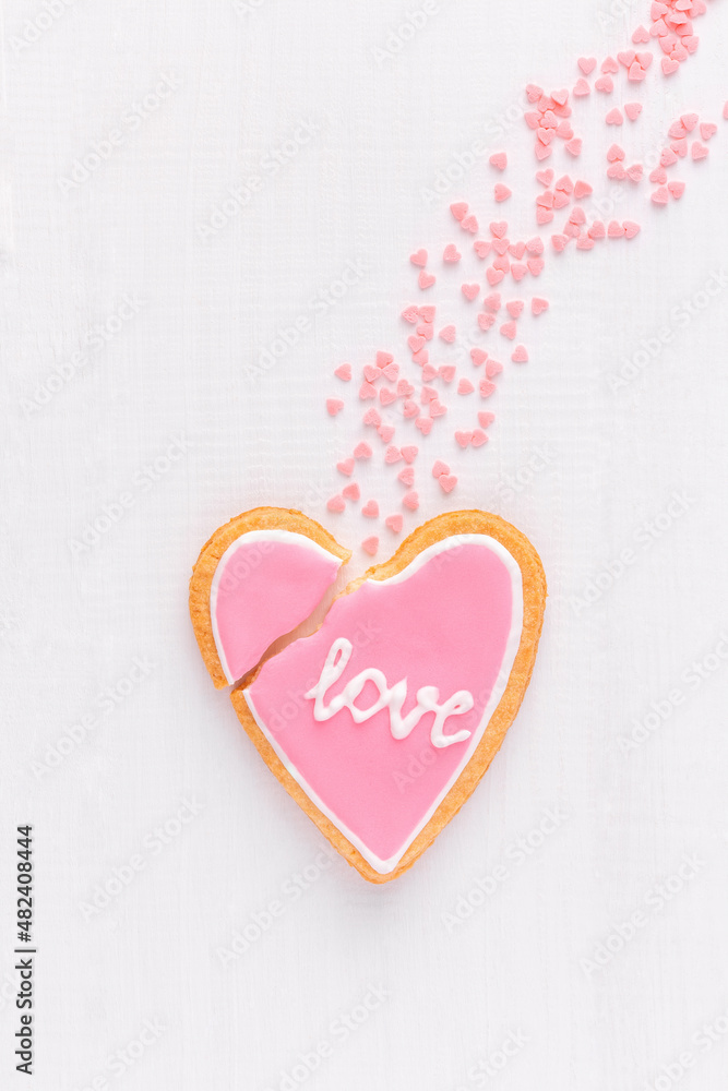 Broken heart shaped cookie with text LOVE is falling down like a comet, top view, flat lay