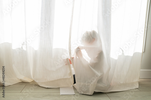 Young child hiding behind a curtain at home
