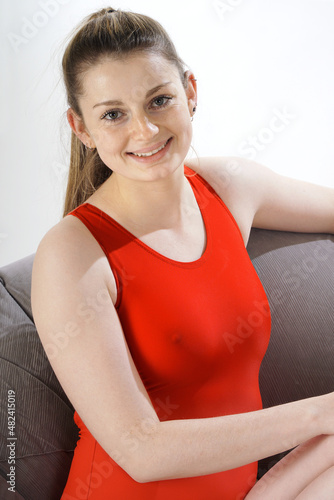 Obraz na płótnie Beautiful young woman in red one piece swimsuit posing on a sofa in studio w salonie
