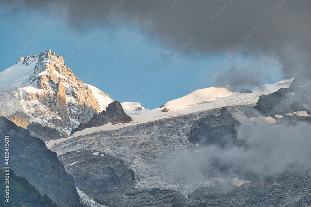 The massif of the Mont Blanc, as seen from Chamonix, Haute Savoie, France, with a sunlit peak, dark clouds and a glacier
