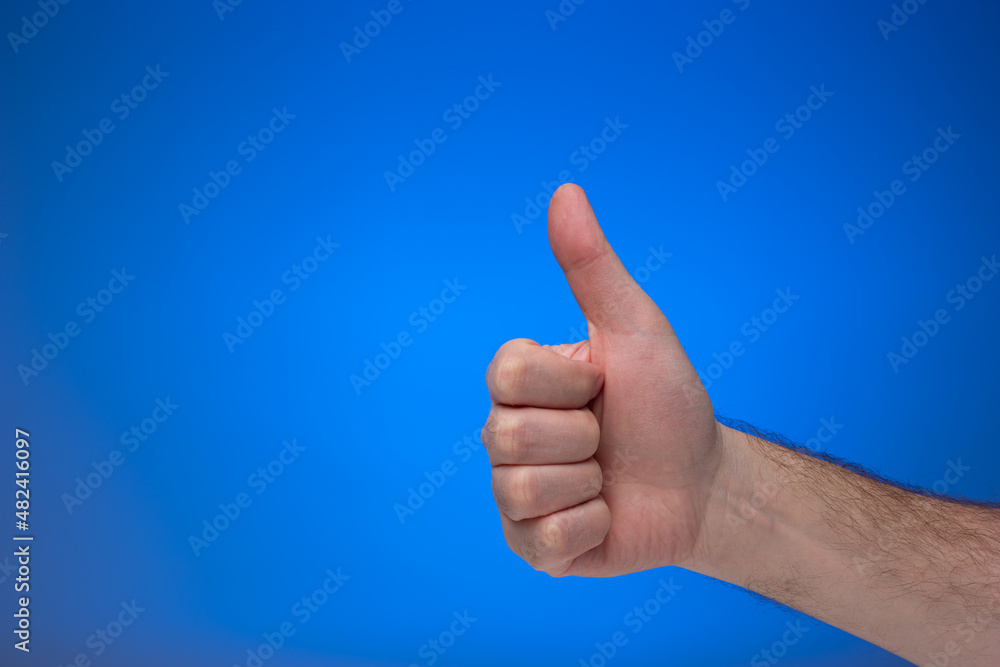 Thumb's up like gesture made by Caucasian male hand. Close up studio shot, isolated on blue background Thumb's up like gesture made by Caucasian male hand. Close up studio shot, isolated on blue background