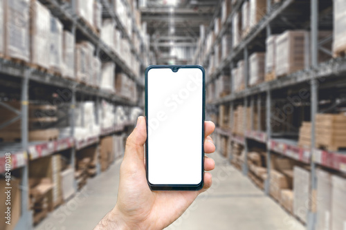 Warehouse with a hand holding an empty smartphone. Blurred industrial warehouse with goods and products. Logistics, business, delivery, services concept photo