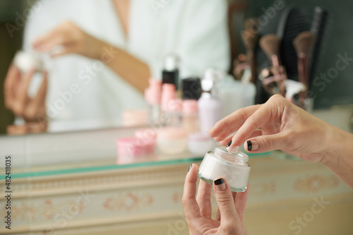 Hands of woman taking rich face cream from glass jar