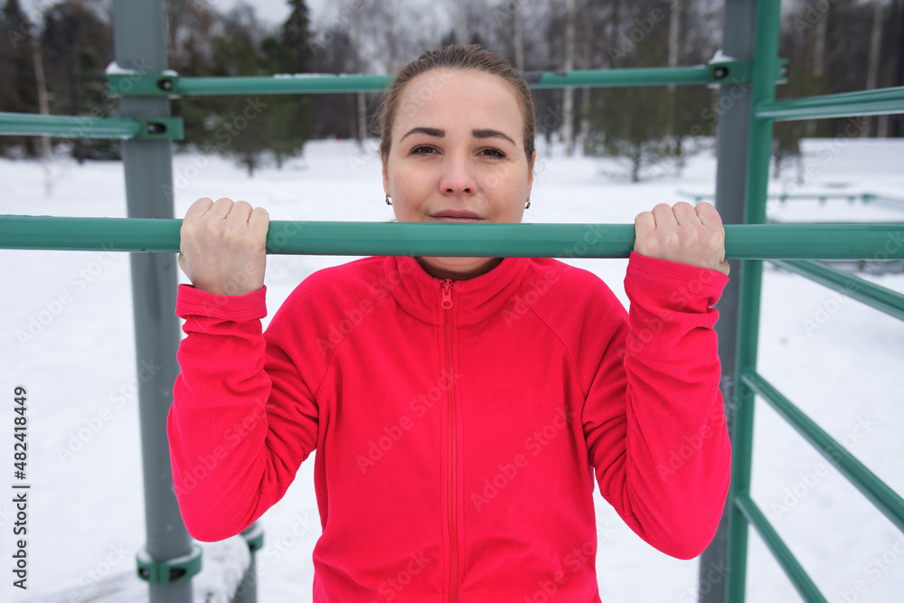 Obraz premium Young beautiful athletic girl, fit fitness active woman is training, workout outdoors, doing pull ups on horizontal bar at snow at winter cold icy frost day. Healthy lifestyle. 