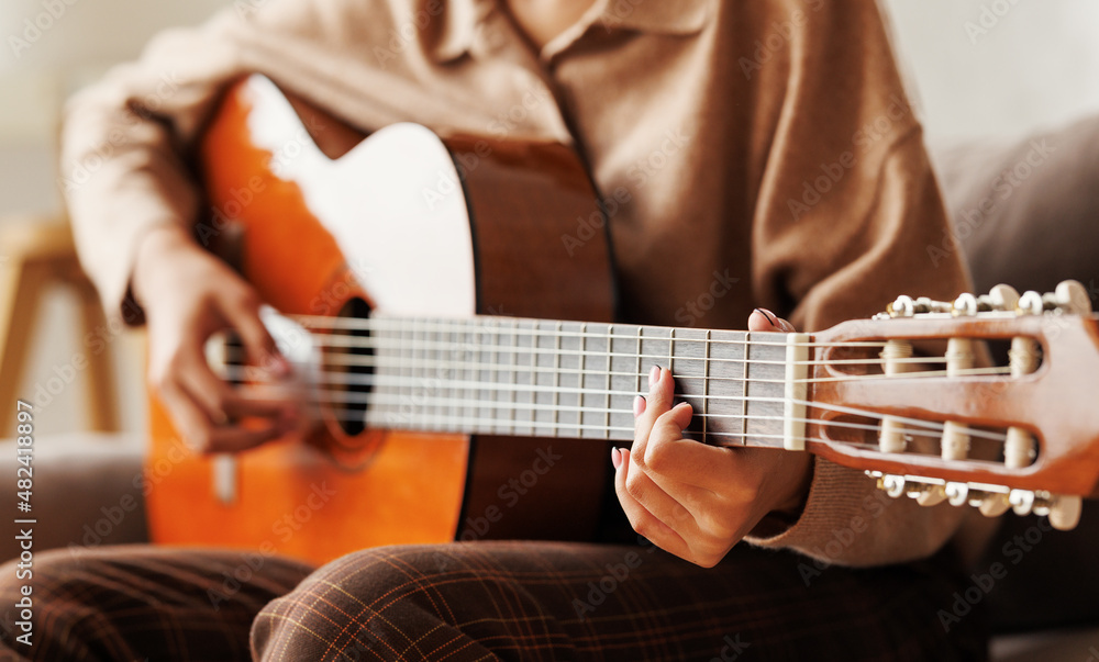 Cropped shot of woman guitarist sitting on sofa at home and playing acoustic guitar