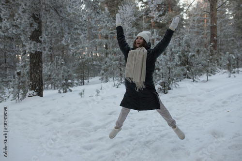 A young girl jumps with an asterisk in a winter snow-covered forest.