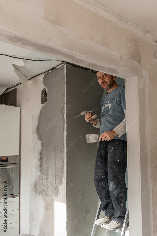 Fototapeta premium A man-a master of European appearance plasters the walls, makes repairs in the apartment, the concept of repairing and remodeling the house