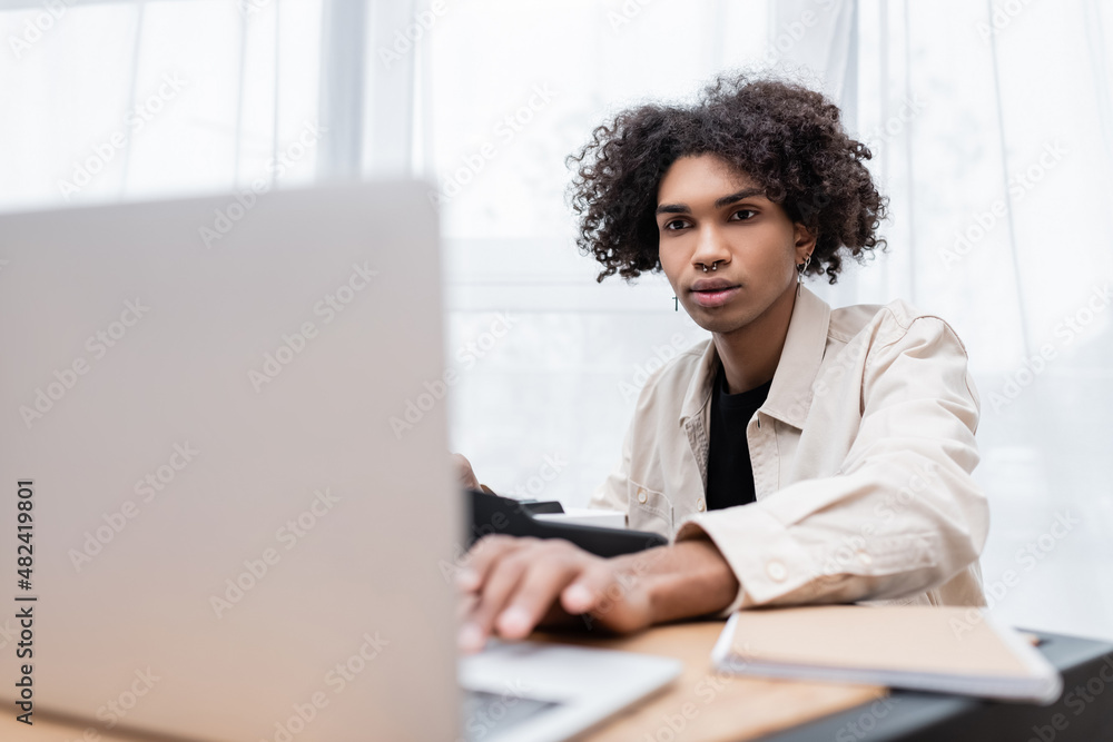 Young african american man using laptop and playing synthesizer at home. Young african american man using laptop and playing synthesizer at home.