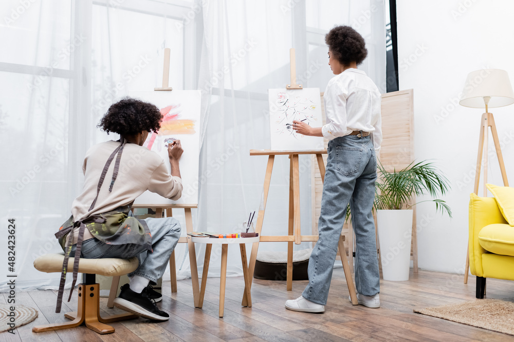 Fototapeta premium African american couple painting on canvases in living room.