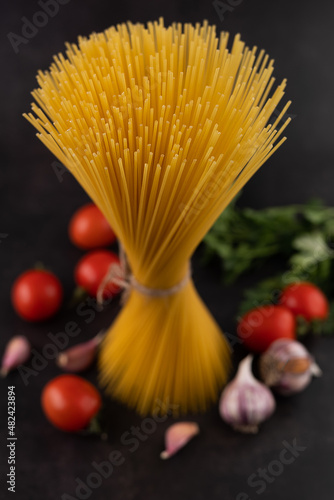 Blurred image of a bunch of spaghetti with tomatoes, garlic and herbs on a black background.