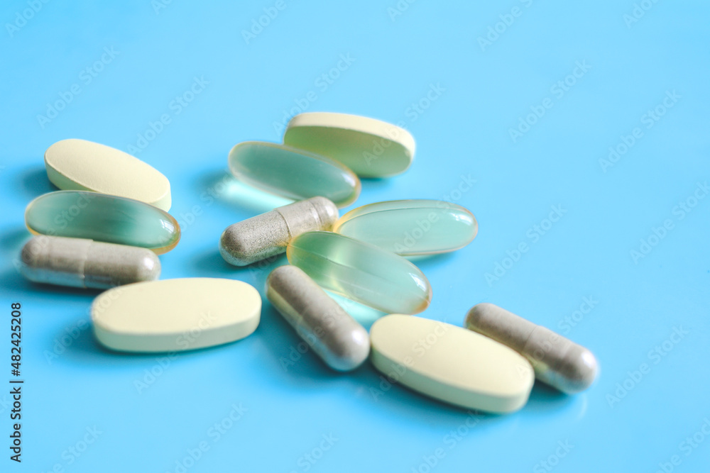 Amber color gel medicine capsules and yellow supplement nutrient pills on blue background, pharmaceutical medical and healthcare concept. Amber color gel medicine capsules and yellow supplement nutrient pills on blue background, pharmaceutical medical and healthcare concept.