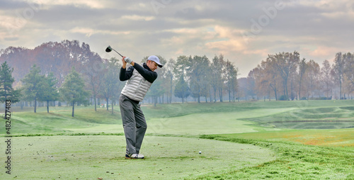 Golfer on a golf course in winter with fog and frost, on the starting tee. Golfer with golf club hitting the ball for the perfect shot.