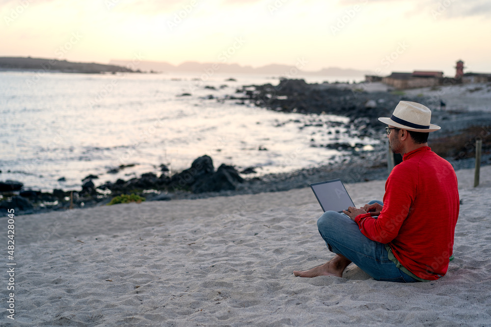 man sitting on the beach outdoor with a laptop alone doing telecommuting or remote work