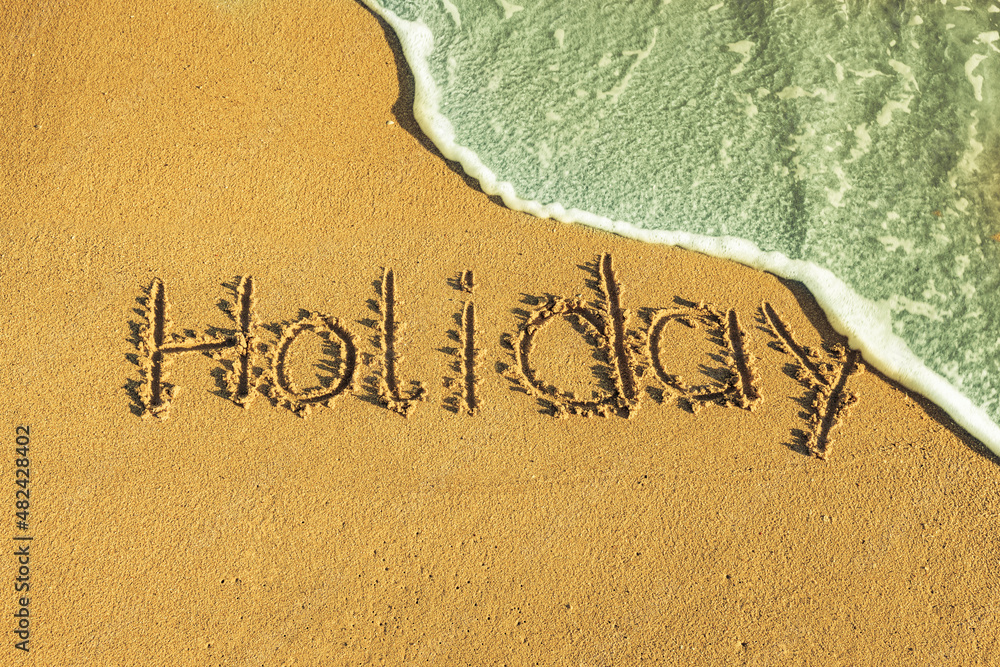 Fototapeta premium Das Wort holiday in den Sand geschrieben