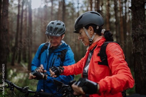 Senior couple bikers setting smartwatch outdoors in forest in autumn day.