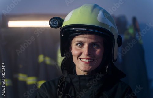 Happy mid adult female firefighter looking at camera indoors in fire station at night. © Halfpoint