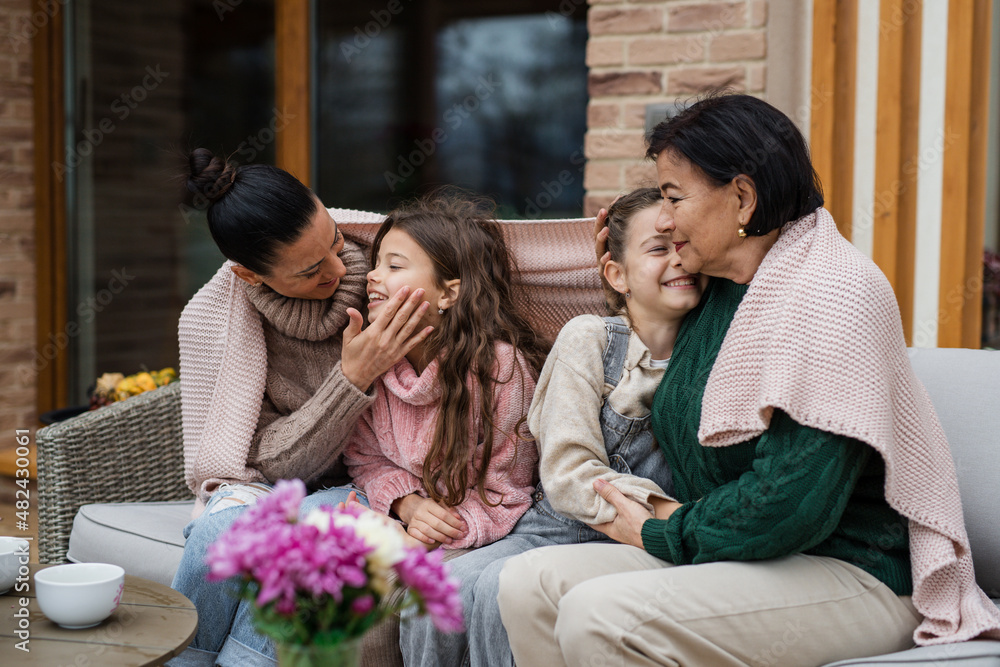 Two happy sisters with mother and grandmother sitting wrapped in blanket outdoors in patio in autumn Two happy sisters with mother and grandmother sitting wrapped in blanket outdoors in patio in autumn