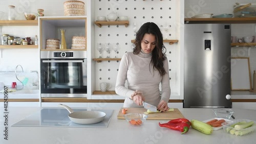 Young vegan woman cooking vegetarian meal in her apartment on modern domestic kitchen cook top. Female preparing food for lunch or dinner, she invited guests at her new home.