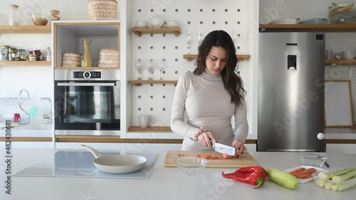 Young vegan woman cooking vegetarian meal in her apartment on modern domestic kitchen cook top. Female preparing food for lunch or dinner, she invited guests at her new home.