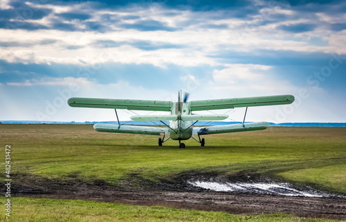 An-2 aircraft before takeoff at a dirt airfield against a sky with clouds in summer