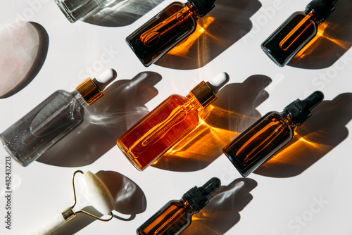 A set of many different glass bottles with cosmetic liquids arranged in a row. The play of light creates abstract patterns of shadows. 