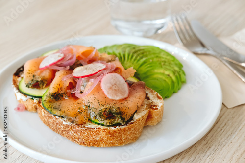 Salmon toast with avocado and vegs in the modern cafe. Fancy cafe and modern healthy snack concept. Take away, delivery menu item