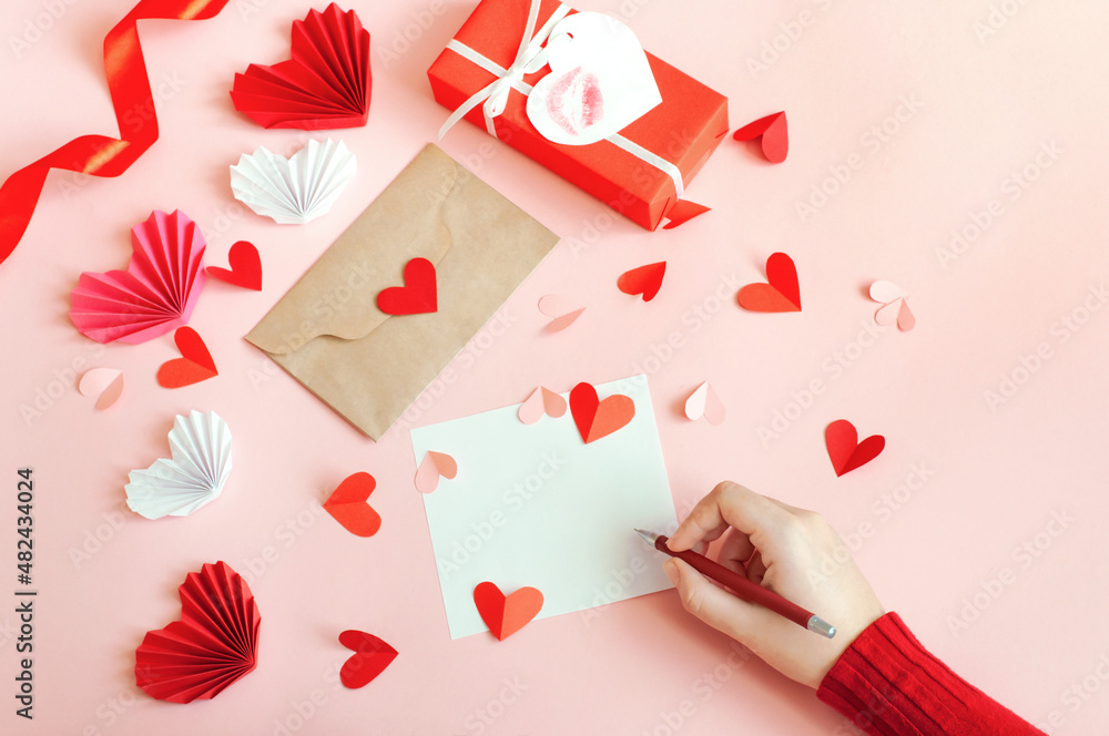 Valentine's Day, a girl writes a love message on a pink background with paper hearts and a gift. High quality photo Valentine's Day, a girl writes a love message on a pink background with paper hearts and a gift. High quality photo