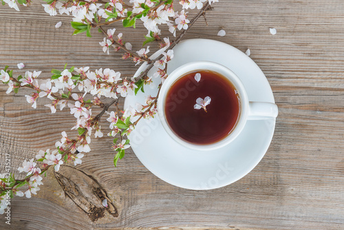Spring tea time; white cup of tea or coffee and cherry blossom on wooden table; top view