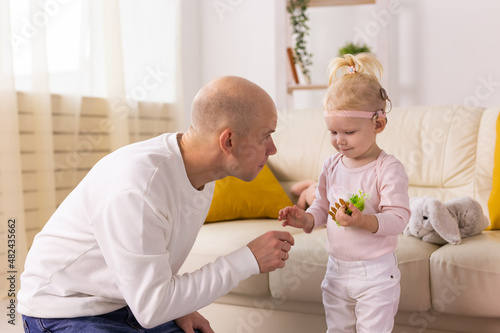 Child with cochlear implants having fun with father at home. Deafness and medical technology concept.