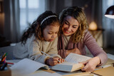Little multiracial girl doing homework with her mother in evening at home.