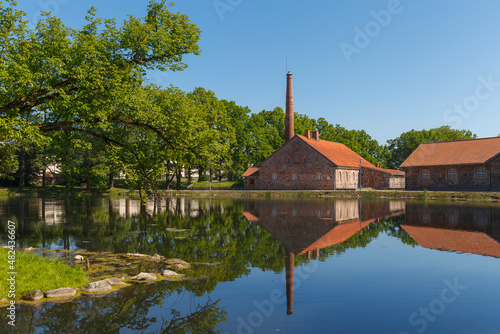 An old Olustvere manor in the summer time. The manor's vodka factory buildings are reflected in the park's pond. Estonia.