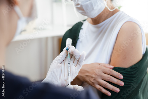 People getting a vaccination to prevent pandemic concept. Mature Woman in medical face mask receiving a dose of immunization coronavirus vaccine from a nurse at the medical center hospital
