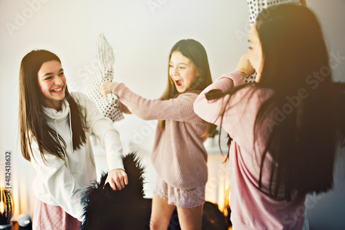 Three excited teenager girls having fun together enjoying laze leisure time with pillow fight