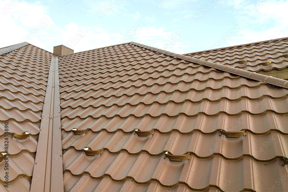 Detail view of house rooftop covered with brown metal tile sheets. Detail view of house rooftop covered with brown metal tile sheets.