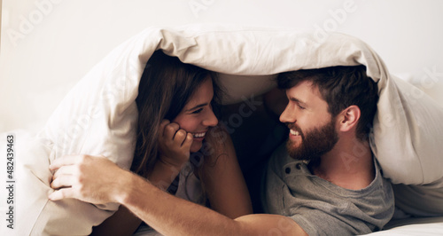 Weekends were made for comfort. Shot of a happy young couple covering themselves with a blanket on the bed at home.