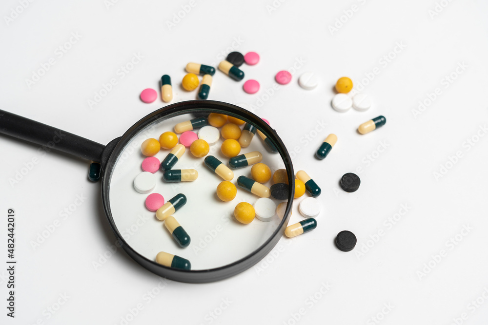creative pharmacy and health layout, magnifying glass on top of medicine pills tablets and capsules creative pharmacy and health layout, magnifying glass on top of medicine pills tablets and capsules