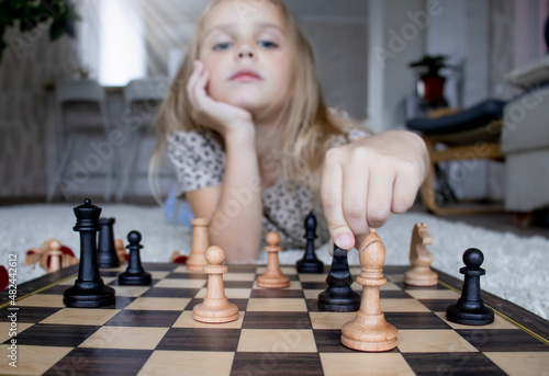 selective focus on chessboard and wooden chess pieces, little girl with a chess piece in her hand, strategy games at home, additional education for children